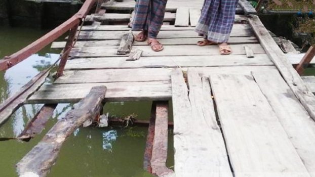 People cross canal by broken wooden bridge taking risk